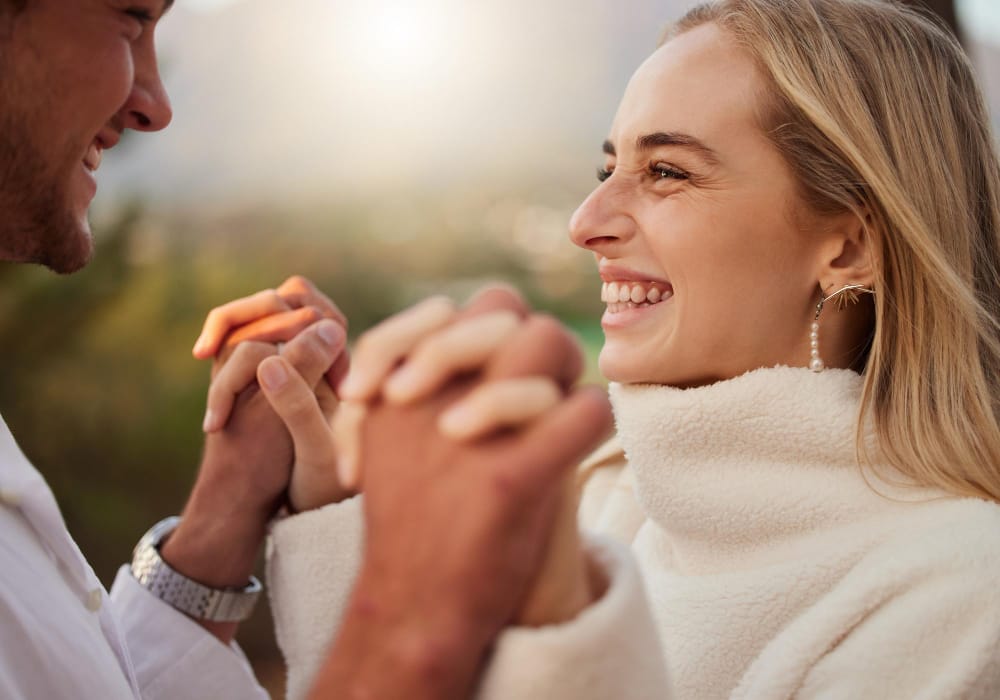 A smiling young woman holding hands with her husband outdoors in warm evening light.