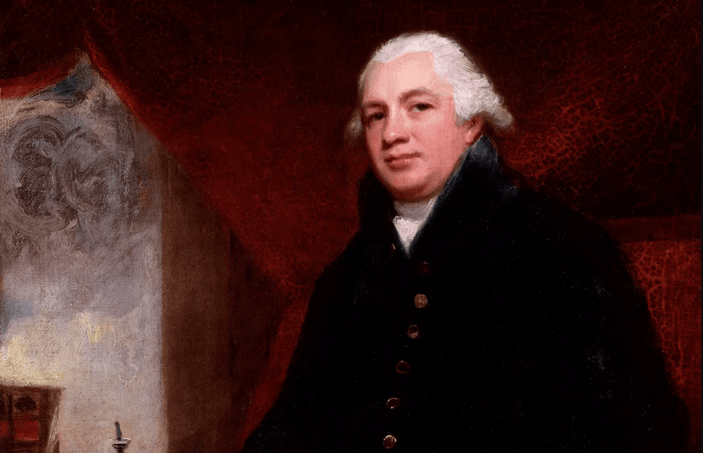 Portrait of Robert Raikes, founder of the Sunday school movement, in a dark coat and white wig against a red curtain.