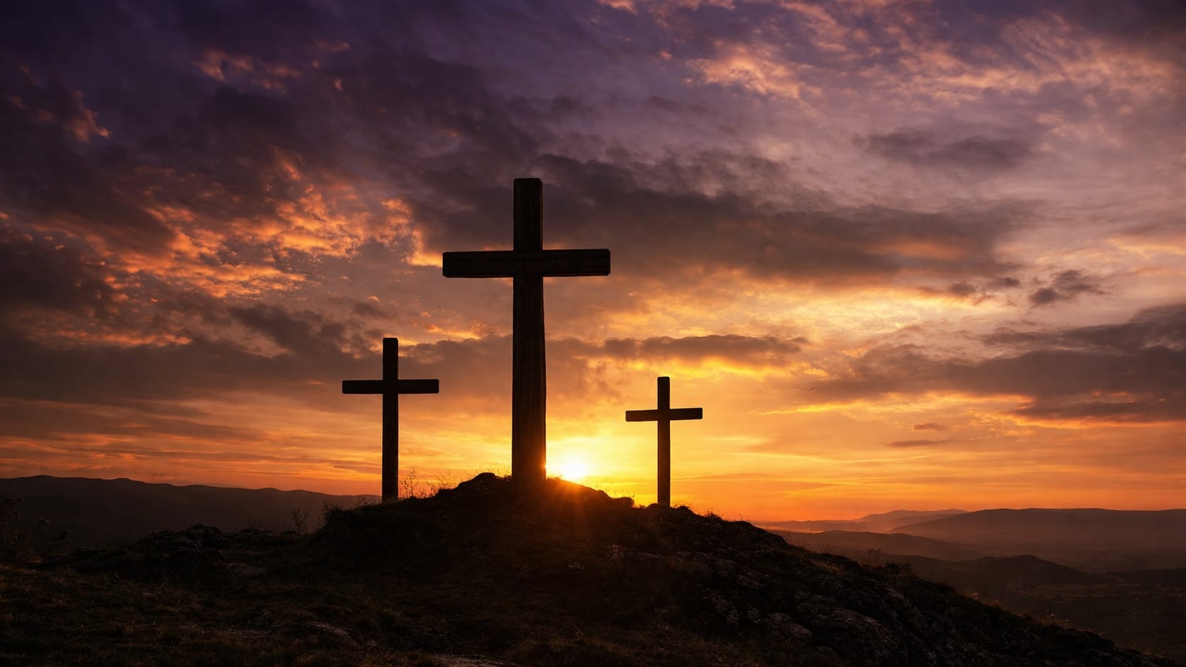 Three crosses silhouetted on a hilltop against an orange and purple sunset.